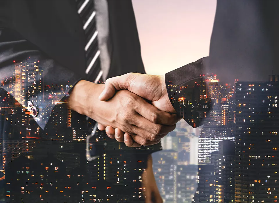 Double exposure image of business people handshake on city office building in background showing partnership success of business deal.